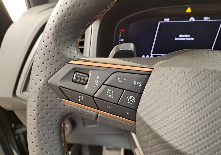 Gros plan sur les commandes du volant perforé du CUPRA Ateca 2024 noir magique, avec surpiqûres cuivrées et détails carbone.