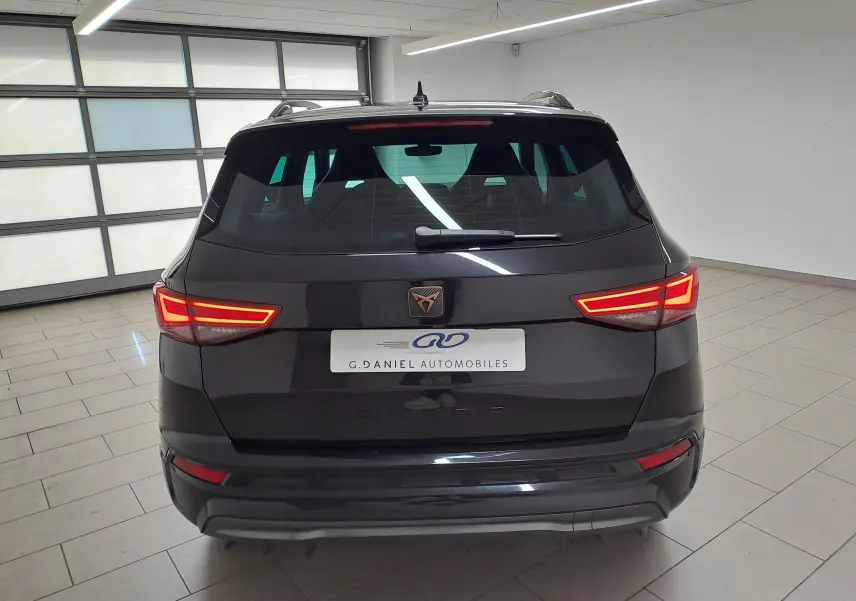Vue arrière d’un CUPRA Ateca 2024 noir magique avec feux LED allumés dans un garage lumineux.