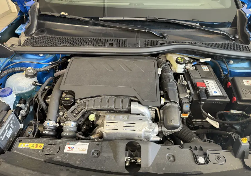 Vue rapprochée du moteur essence d'une Peugeot 2008 bleu Vertigo avec capot ouvert, montrant les composants du compartiment moteur.