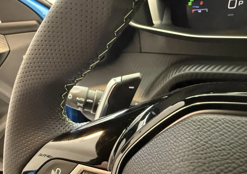 Gros plan sur le volant perforé et les commandes du tableau de bord d'une Peugeot 2008 GT bleu Vertigo métal.