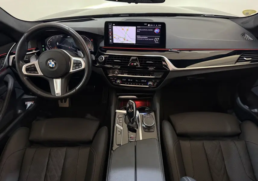 Vue intérieure avant de la BMW Série 5 Touring 520d M Sport 2023, tableau de bord noir avec écran tactile et volant cuir alu.