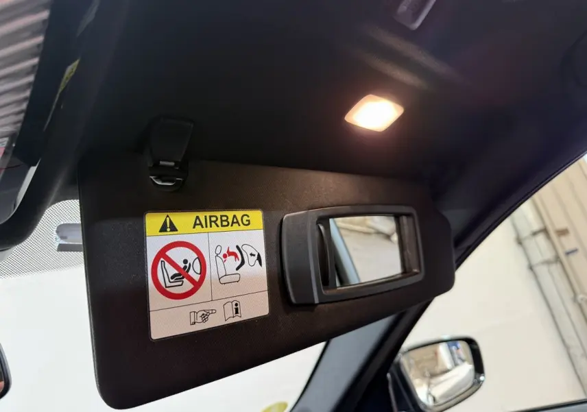 Détail du pare-soleil côté conducteur avec miroir intégré et avertissement airbag dans l’habitacle noir.
