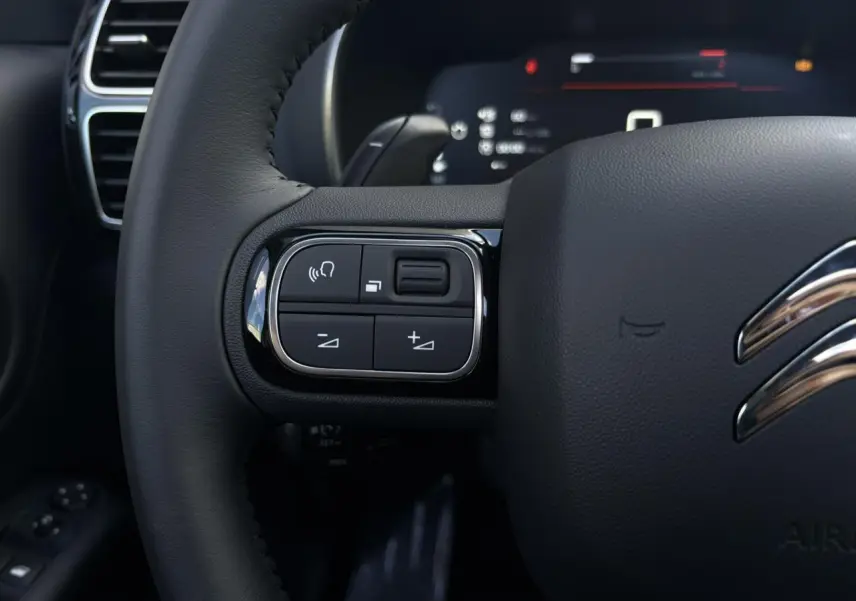 Gros plan sur les commandes gauche du volant en cuir noir du Citroën C5 Aircross 2026, tableau de bord numérique en arrière-plan.