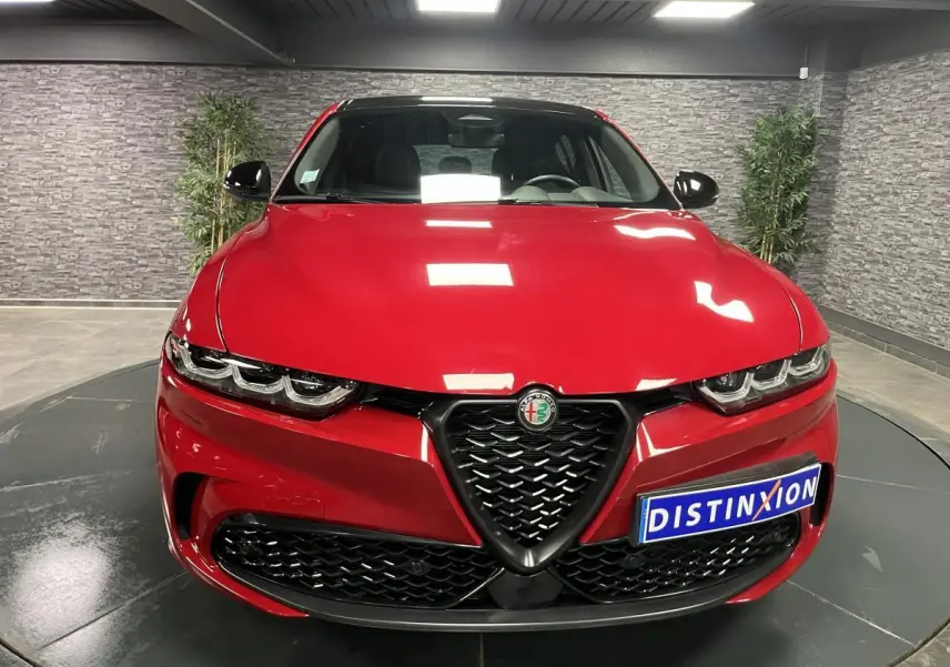 Vue frontale d'une Alfa Romeo Tonale rouge avec calandre noire en V et phares LED distinctifs dans un showroom.