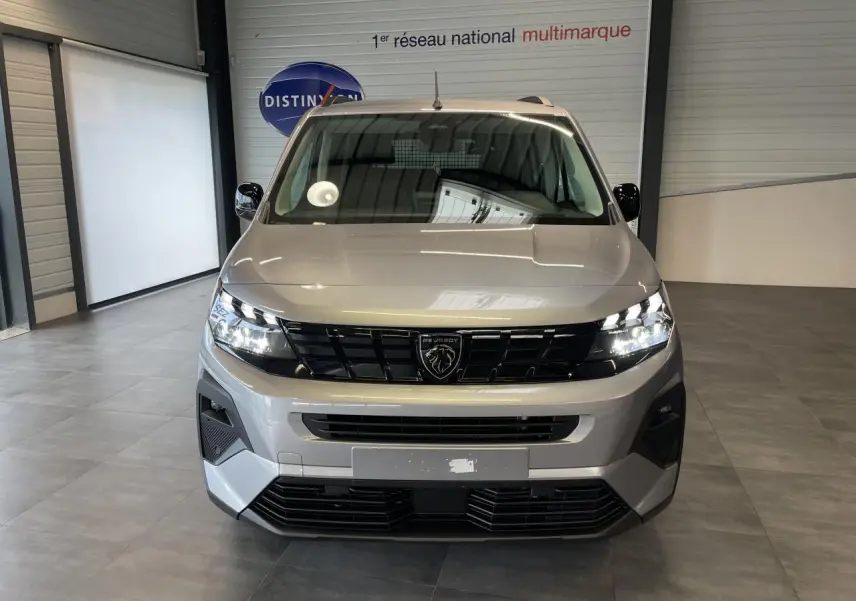 Vue frontale du Peugeot Rifter gris Artense avec calandre noire et signature lumineuse LED allumée en intérieur showroom.
