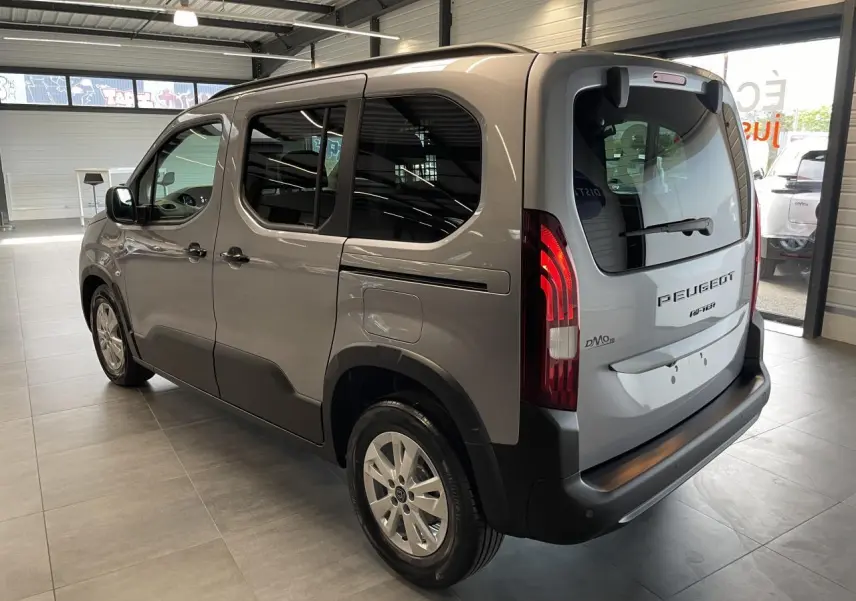 Vue 3/4 arrière droit du Peugeot Rifter gris Artense en showroom, avec portes latérales coulissantes et feux arrière allumés.
