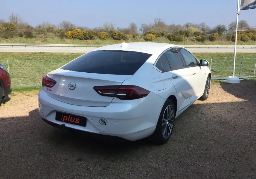 Opel Insignia Grand Sport blanc nacré vue 3/4 arrière droit, avec vitres teintées et jantes alliage.