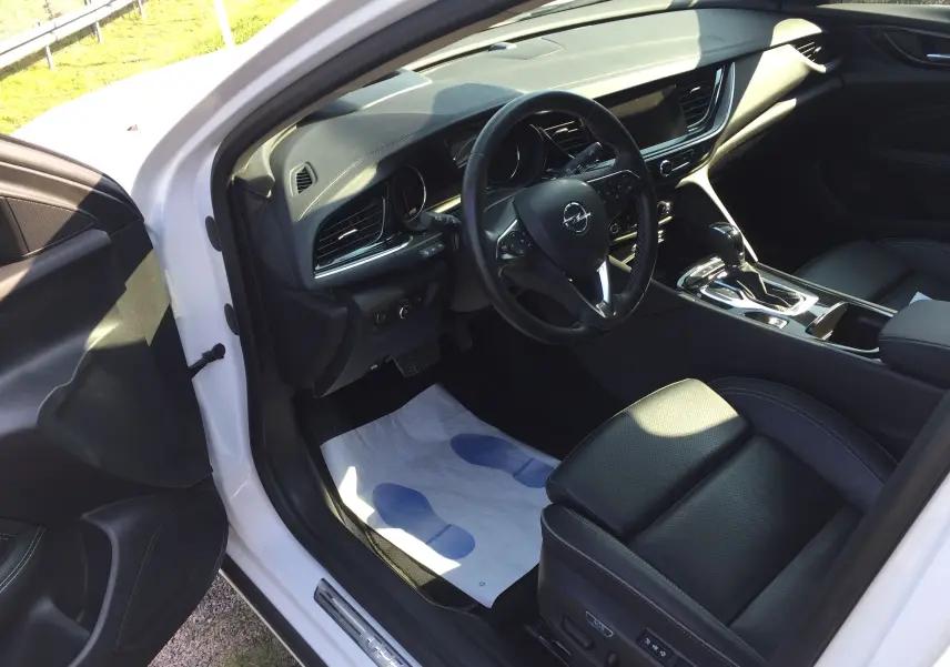 Vue intérieure côté conducteur de l'Opel Insignia Grand Sport blanc nacré, avec sièges cuir noirs et tableau de bord moderne.