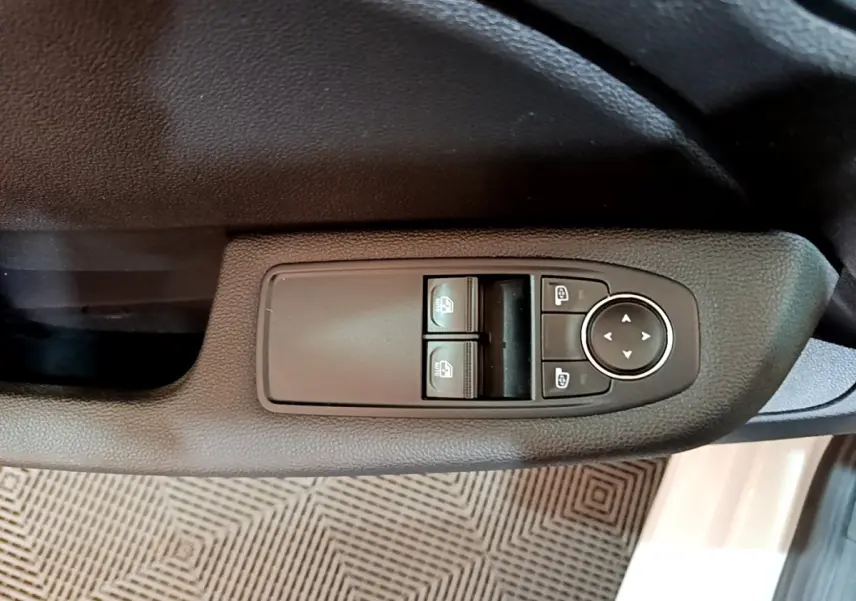 Vue rapprochée des commandes de lève-vitres et réglage des rétroviseurs côté conducteur d’une Renault Clio blanche.
