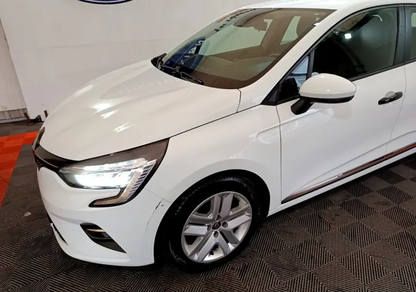 Vue 3/4 avant droit d'une Renault Clio Business blanche avec phares LED allumés et jantes alliage.