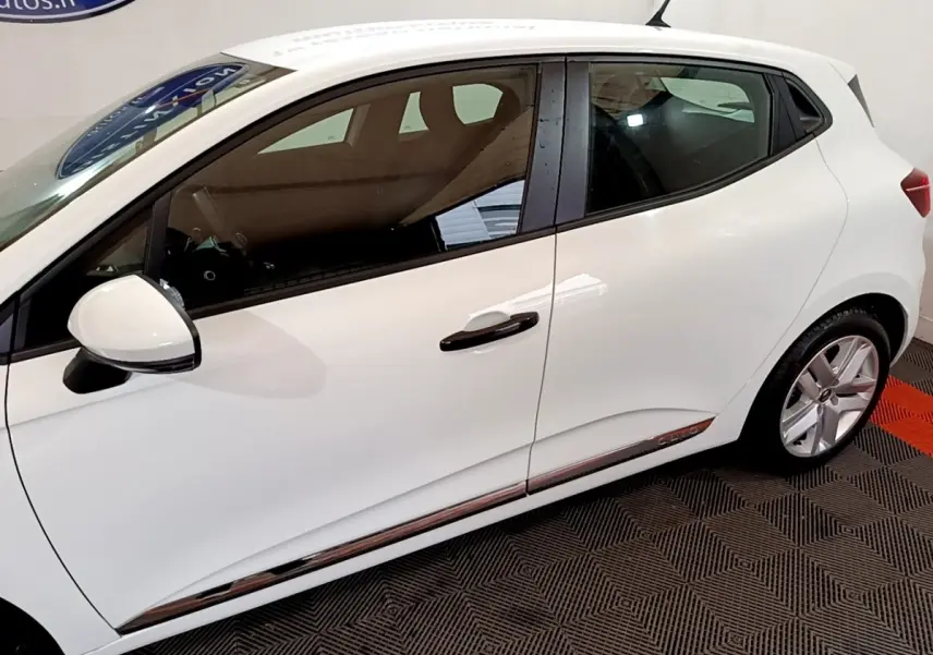 Profil droit d'une Renault Clio Business blanche, avec poignées et rétroviseur noir, sur sol à damiers noir et rouge.