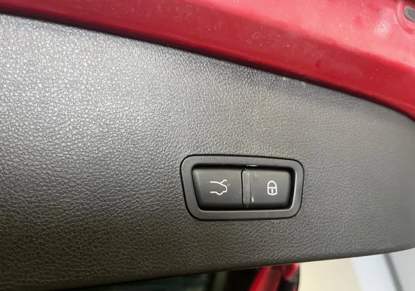 Gros plan sur le panneau intérieur rouge du coffre avec boutons d’ouverture et de verrouillage sur Alfa Romeo Tonale rouge.