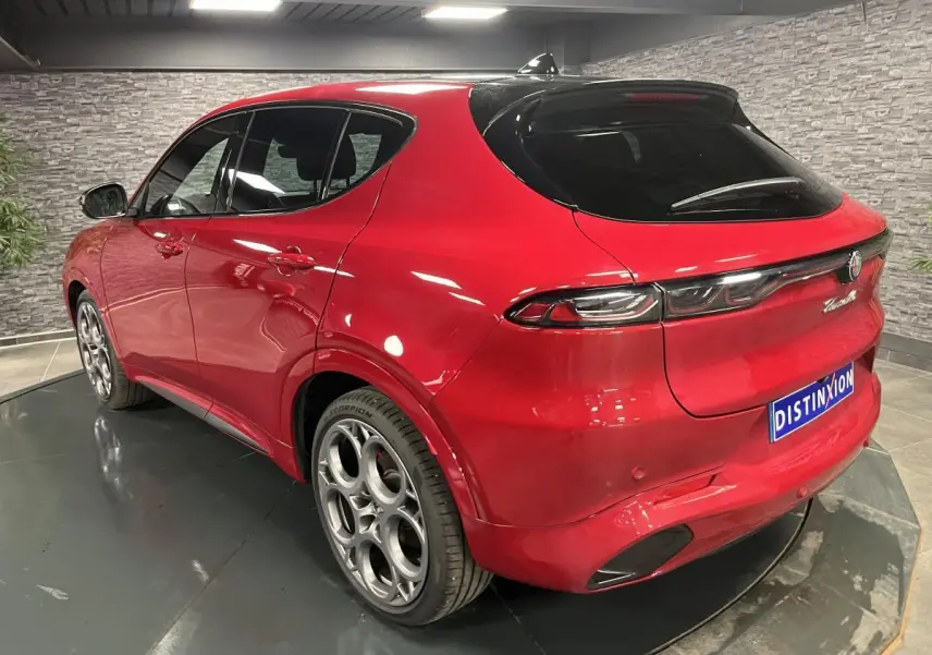 Vue 3/4 arrière droite de l'Alfa Romeo Tonale rouge avec jantes alliage 20 pouces et toit noir en intérieur showroom.