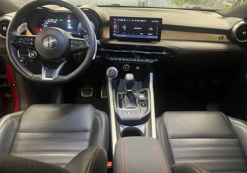 Vue intérieure avant de l'Alfa Romeo Tonale 2024, volant sport cuir noir, écran tactile et inserts carbone sur tableau de bord.