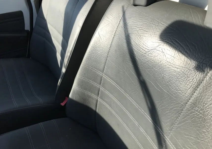 Gros plan sur les sièges avant en cuir noir du Citroën C15 Isotherm blanc de 1997, vue intérieure côté conducteur.