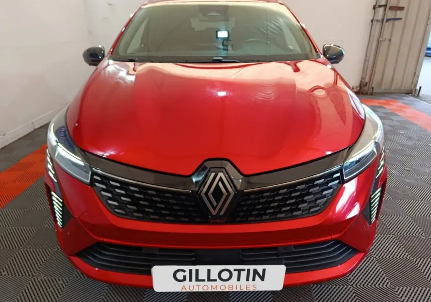 Vue avant d'une Renault Clio Techno TCe 90 rouge avec calandre noire et feux LED allumés dans un garage.