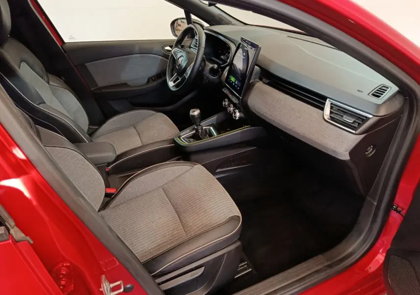 Vue intérieure côté conducteur de la Renault Clio Techno TCe 90 rouge 2024 avec tableau de bord moderne et boîte manuelle.