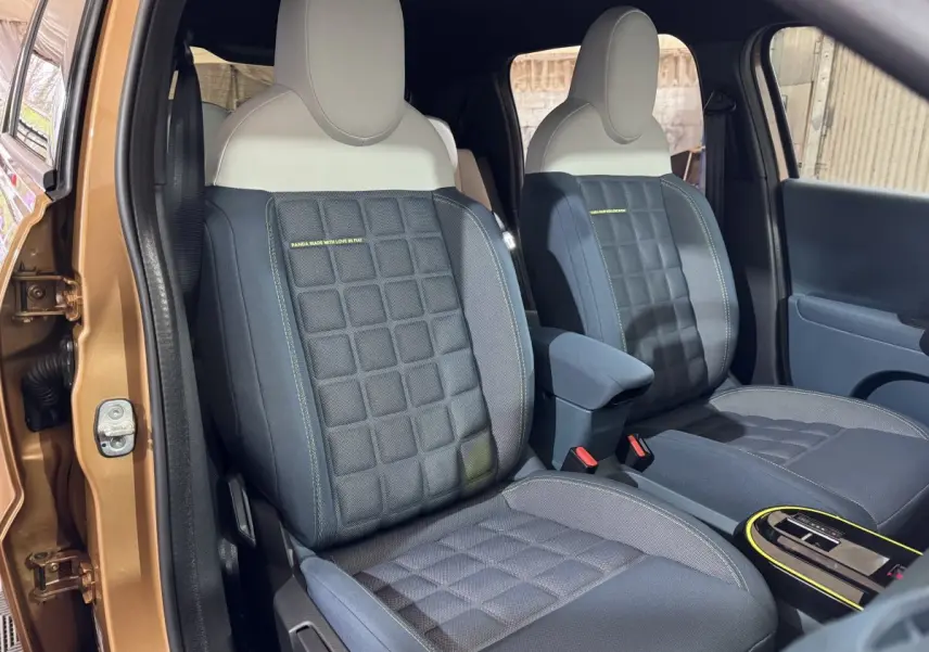 Vue intérieure des sièges avant bleu foncé et beige de la FIAT Grande Panda marron, porte ouverte côté gauche.