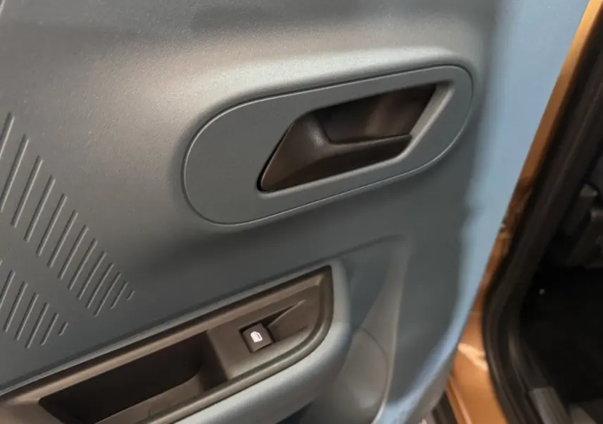 Gros plan sur la poignée intérieure et le bouton de lève-vitre côté droit d'une Fiat Grande Panda marron.