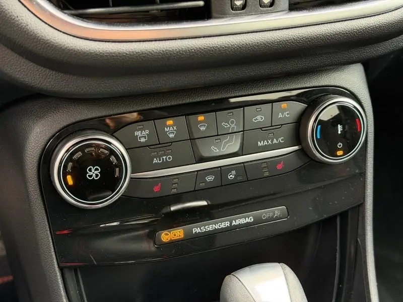 Vue rapprochée de la console centrale noire du Ford Puma 2024, avec commandes climatisation et sièges chauffants allumées.
