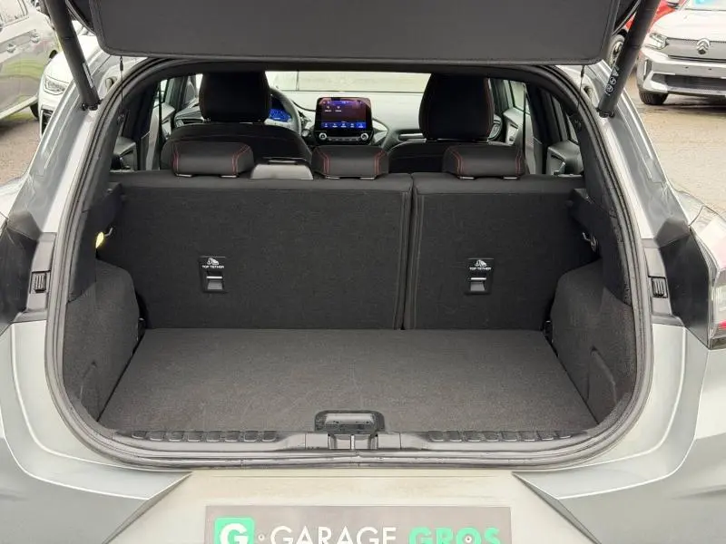 Coffre ouvert d’un Ford Puma gris Solar métallisé, vue de l’arrière montrant banquette arrière et tableau de bord avec écran tactile.
