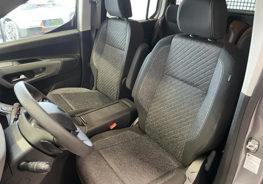 Vue intérieure sur les sièges avant en tissu gris du Peugeot Rifter 2026, avec accoudoirs et volant multifonction cuir.