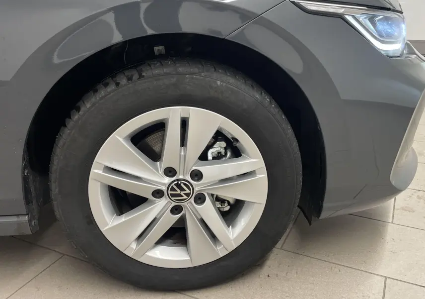 Gros plan sur la roue avant gauche et le phare d'une Volkswagen Golf 2024 gris dauphin métallisé.