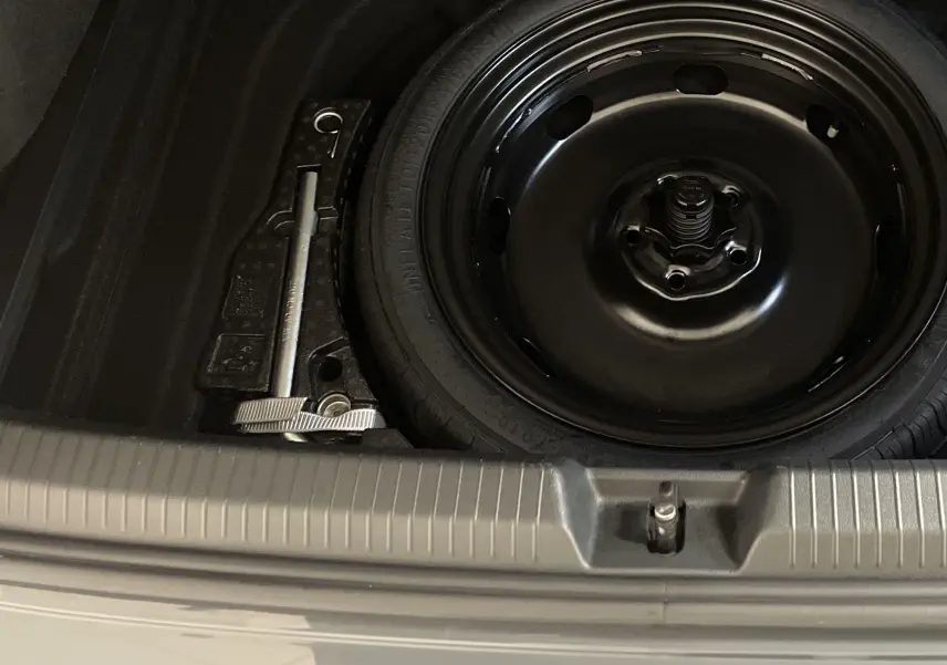 Gros plan sur la roue de secours noire et le cric dans le coffre d'une Volkswagen Golf Gris Dauphin 2024.
