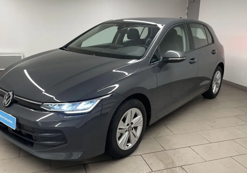 Volkswagen Golf 1.5 TSI Gris Dauphin vue 3/4 avant droit avec phares allumés en intérieur showroom.