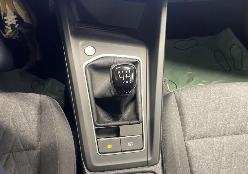 Le levier de vitesses manuel noir de la Volkswagen Golf 2024 vu de dessus entre les sièges gris.