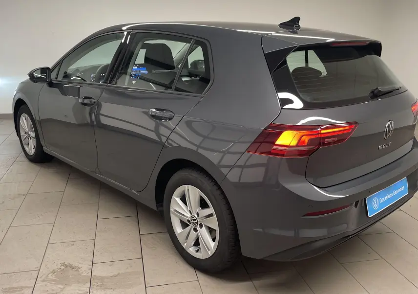 Volkswagen Golf 1.5 TSI gris dauphin vue 3/4 arrière droit en intérieur avec feux arrière allumés.