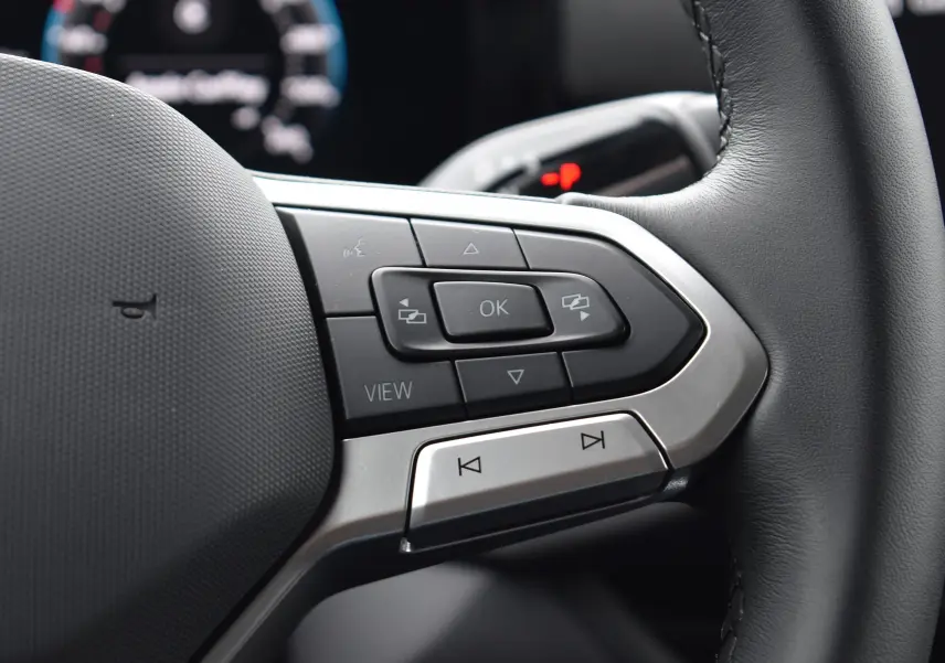 Gros plan sur les commandes multifonctions en aluminium et cuir du volant du Volkswagen T-Roc blanc 2025.