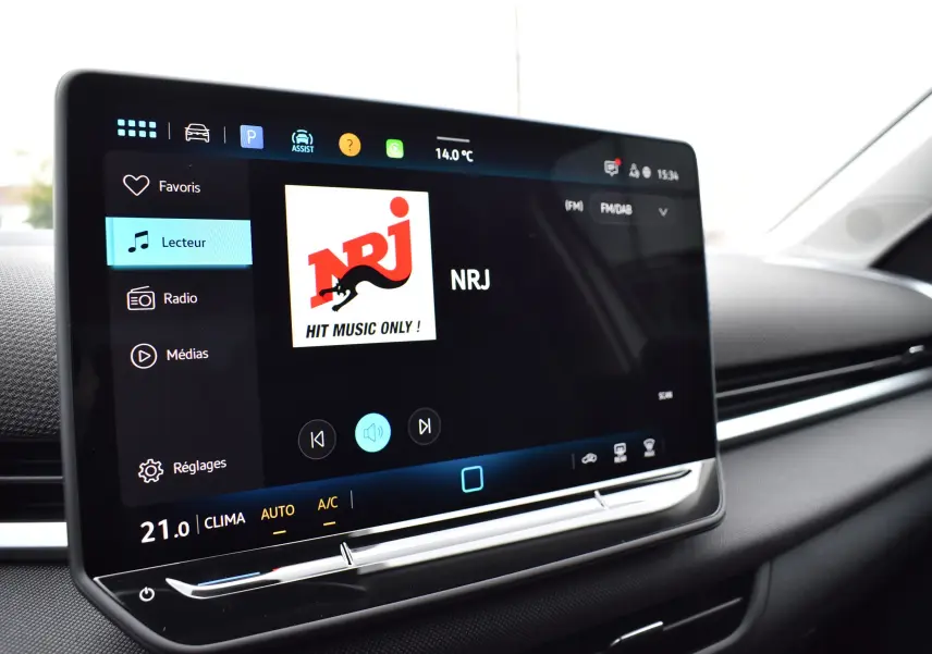 Écran tactile central du Volkswagen T-Roc 2025 affichant la radio NRJ dans un intérieur noir.