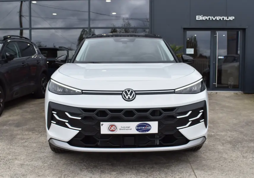 Vue frontale d'un Volkswagen T-Roc blanc 2025 avec calandre noire hexagonale et feux LED fins.