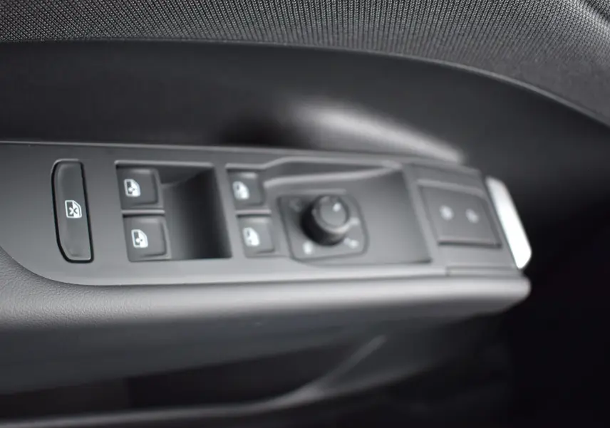 Gros plan sur les commandes des vitres et rétroviseurs côté conducteur du Volkswagen T-Roc blanc, intérieur noir.