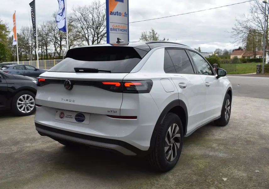 Vue 3/4 arrière droite du Volkswagen T-Roc blanc 2025 avec feux arrière LED et toit noir contrasté.