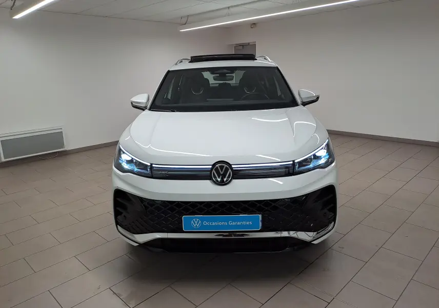 Vue avant d'un Volkswagen Tiguan blanc pur avec phares LED allumés et calandre R-Line dans un showroom.
