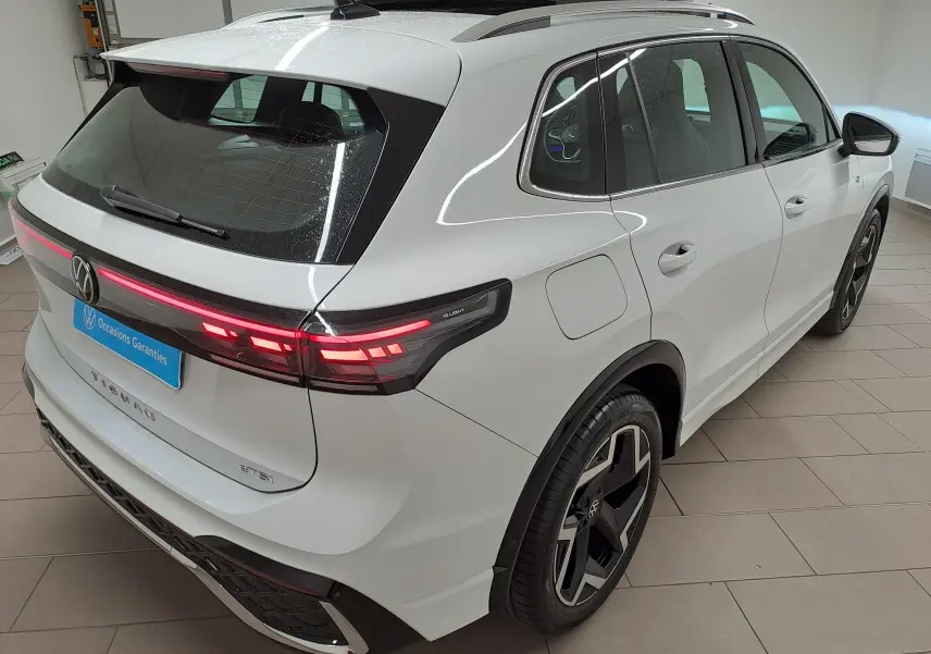 Vue 3/4 arrière droite du Volkswagen Tiguan blanc pur 2025 avec feux arrière allumés et jantes noires distinctives R-Line.