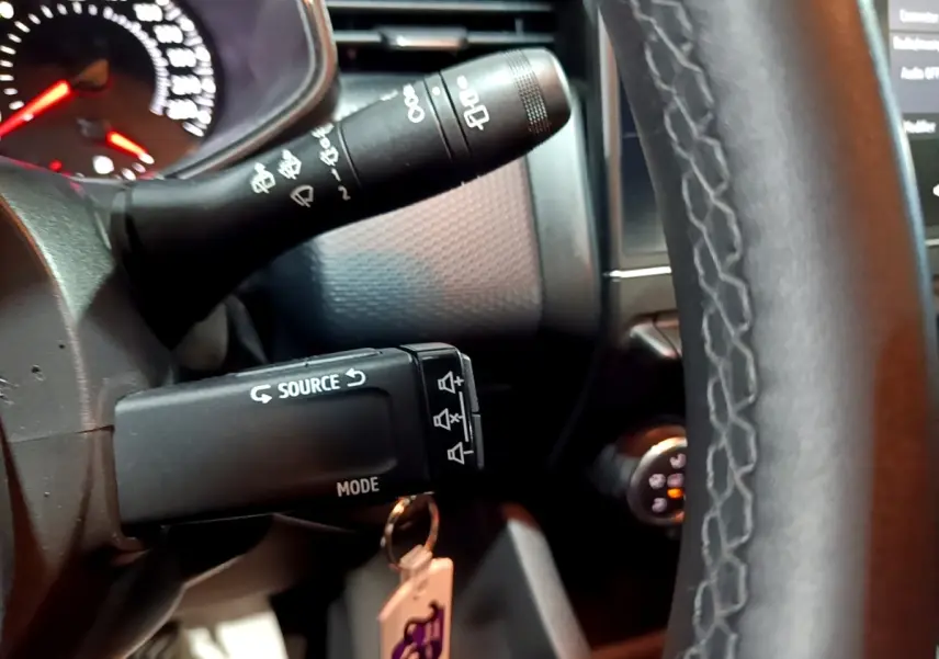 Gros plan sur le volant cuir synthétique et les commandes au volant de la Renault Clio Business bleu, tableau de bord en arrière-plan.