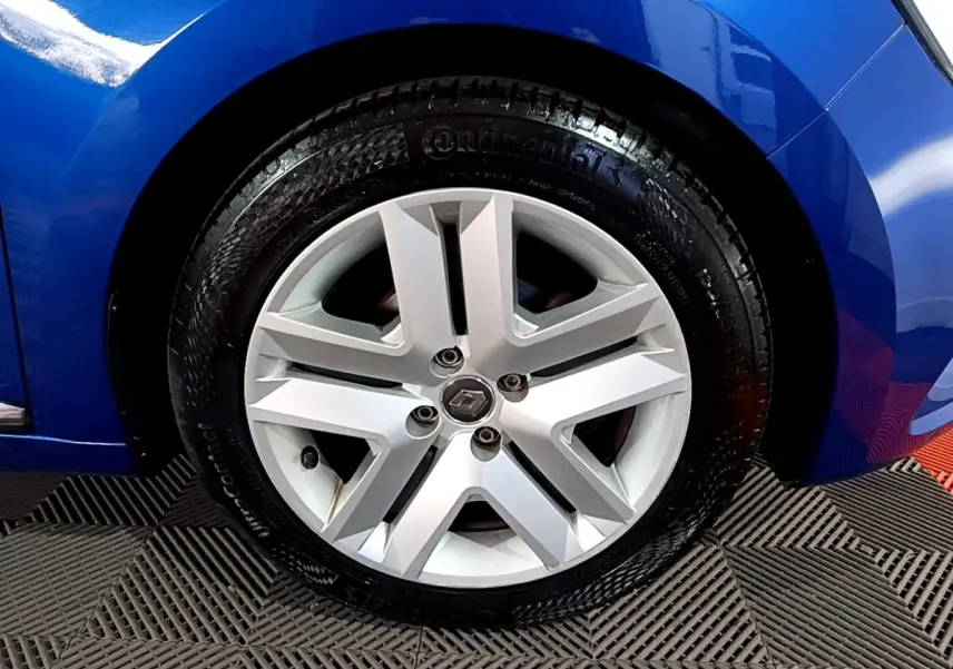 Gros plan sur la roue avant droite d'une Renault Clio Business bleu, avec jante alliage et logo Renault central.