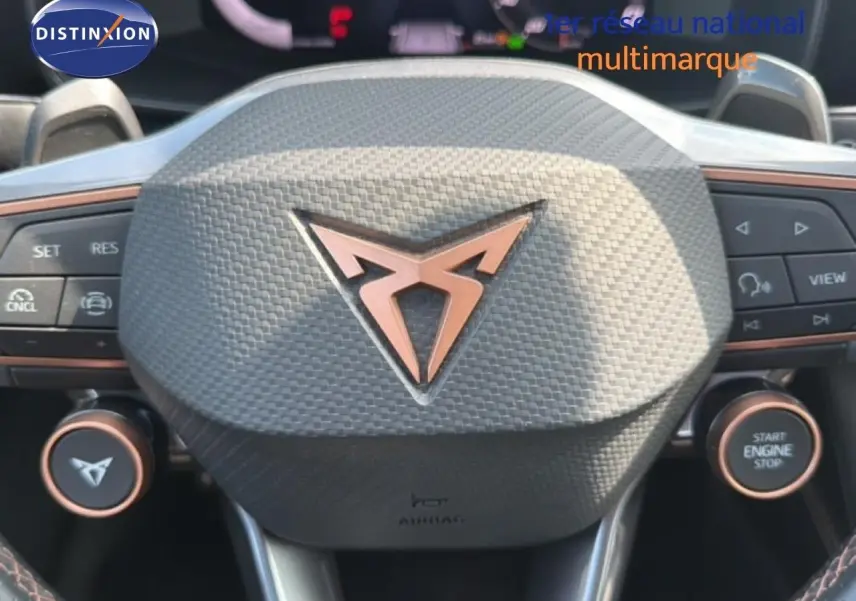 Gros plan sur le volant au design texturé avec logo CUPRA cuivré, boutons multifonctions et démarrage moteur.
