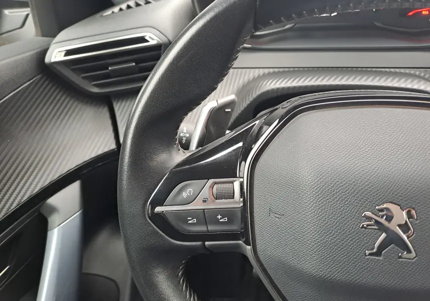 Gros plan sur le volant noir du Peugeot 2008 2020 avec commandes intégrées et tableau de bord à effet carbone.