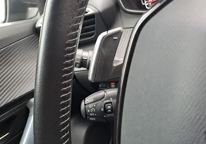 Gros plan sur la commande de régulateur de vitesse et palettes au volant noir du Peugeot 2008 gris Artense 2020.