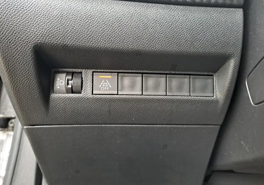 Gros plan sur les commandes de réglage des phares et désactivation de l'alerte de franchissement de ligne d'un Peugeot 2008 gris Artense 2020.