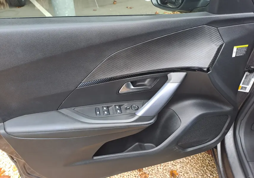 Intérieur de la porte avant gauche d'une Peugeot 2008 gris Artense, avec commandes électriques et insert décoratif noir.