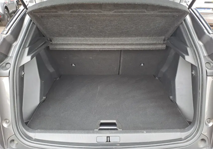 Coffre ouvert vu de l'arrière d'un Peugeot 2008 gris Artense, montrant l'espace de chargement vide et la tablette arrière relevée.