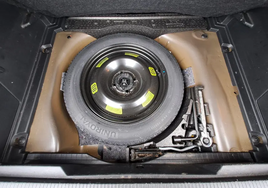 Roue de secours noire et outils de bord dans le coffre du Peugeot 2008 gris Artense, vue plongeante.