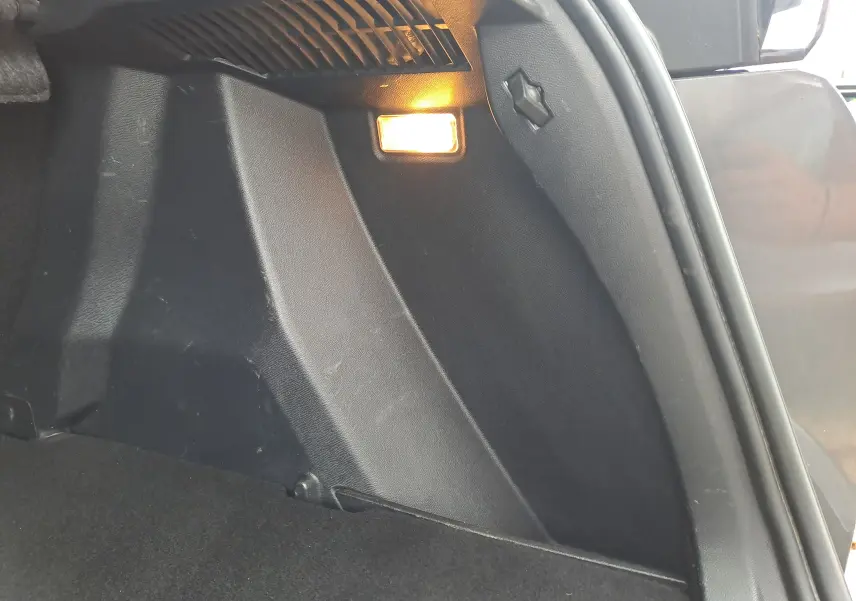 Détail intérieur du coffre côté droit du Peugeot 2008 gris Artense avec éclairage intégré allumé.