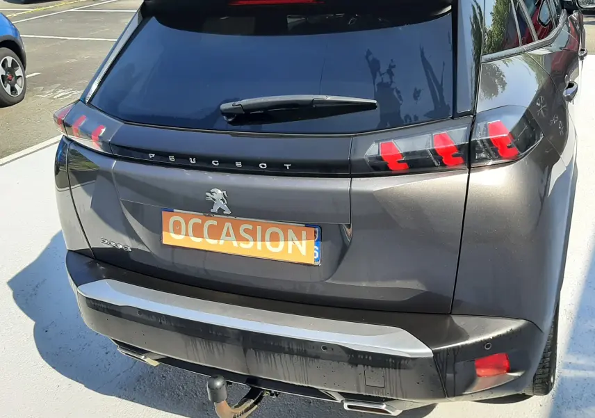 Vue arrière en 3/4 droit d'un Peugeot 2008 gris Artense avec feux LED et attelage visible sur parking.