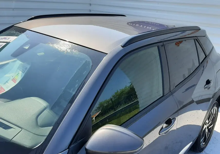 Vue 3/4 avant droit du Peugeot 2008 gris Artense avec toit ouvrant et vitres teintées au soleil.